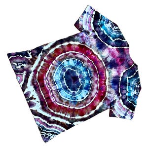 Puede incluir: Una camiseta de manga corta con un patr&oacute;n tie-dye circular de anillos conc&eacute;ntricos en azul profundo, magenta brillante y blanco. El dise&ntilde;o irradia desde el centro, creando un efecto de geoda en toda la tela con acentos de color &iacute;ndigo oscuro.