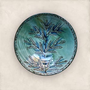 Peut inclure: Un bol rond en céramique turquoise avec un motif d'arbre peint à la main dans des tons de bleu et de noir. Le bol a une bordure décorative et est centré sur un fond neutre. Le bol est une pièce décorative.