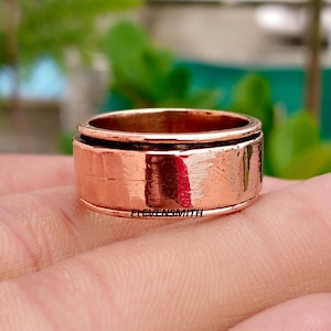 May include: A wide, polished copper spinner ring featuring a smooth, metallic surface with a reflective finish. The band has a distinct central groove separating the outer edges, and the text ELEVENSMITH is clearly engraved on the front surface.