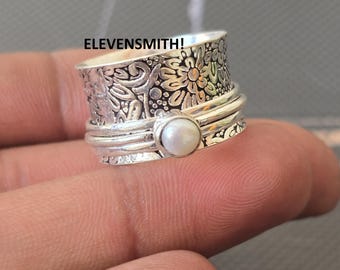 Könnte beinhalten: Ein silberner Spinner-Ring mit floralen und Blattmustern und einer kleinen, runden Perle. Der Ring hat ein strukturiertes Design und der Text "ELEVENSMITH!" ist sichtbar.