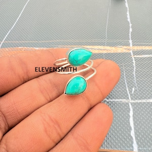 May include: A silver ring featuring two turquoise teardrop-shaped stones. The ring has a spiral design and is shown on a hand. The text "ELEVENSMITH" is visible in the image.