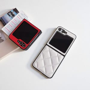 May include: Two phone cases are displayed. One is red and black, resembling a retro television. The other is white with a quilted pattern and black trim. Both cases have a black screen area and are designed for a flip phone.
