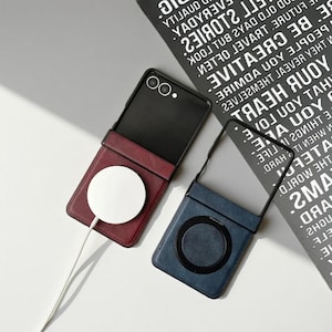 May include: Two phone cases with attached wallets. One is burgundy with a white circular charger, the other is blue with a black circular design. Both cases have a black phone frame. The background has black and white text.