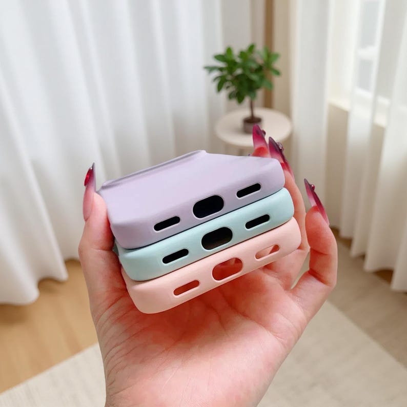 May include: Three pastel-colored phone cases stacked on top of each other. The cases are in shades of lavender, mint green, and peach. Each case has cutouts for the phone's camera and buttons.