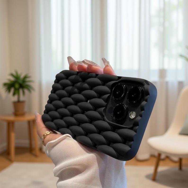 May include: Black phone case with a textured, bubble-like pattern. The case has a raised design and a dark blue border. The phone case has a camera cutout with three lenses.