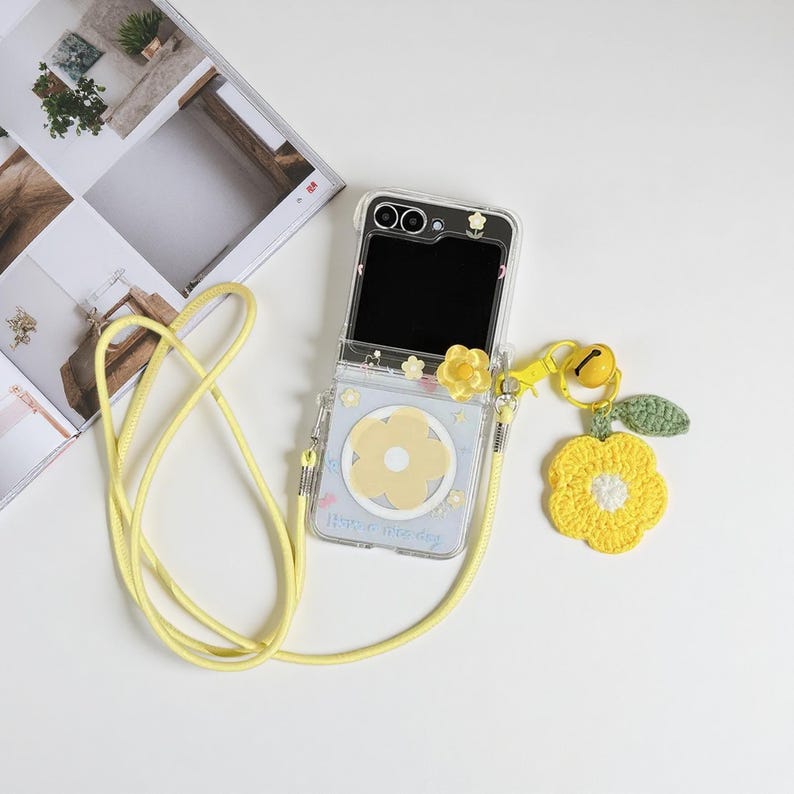 May include: Clear phone case with a yellow flower design and a matching yellow lanyard. The case has a yellow flower charm and a crocheted yellow flower with a green leaf. The phone screen is black. The case says "Have a nice day".