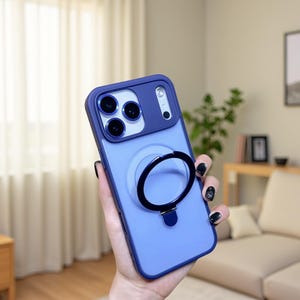 Könnte beinhalten: Eine periwinkelfarbene Handyhülle mit einem dunkelblauen Kameraschutz und einem schwarzen Ringhalter. Die Hülle hat eine glatte Oberfläche und ist für Smartphones konzipiert. Der Ringhalter ermöglicht einen sicheren Halt und kann auch als Ständer verwendet werden.