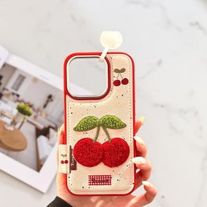 May include: Red and white phone case with a cherry design. The case features a red border, a white background with black speckles, and a 3D cherry design with red cherries and green leaves. The word "Sweet" is printed on the case.