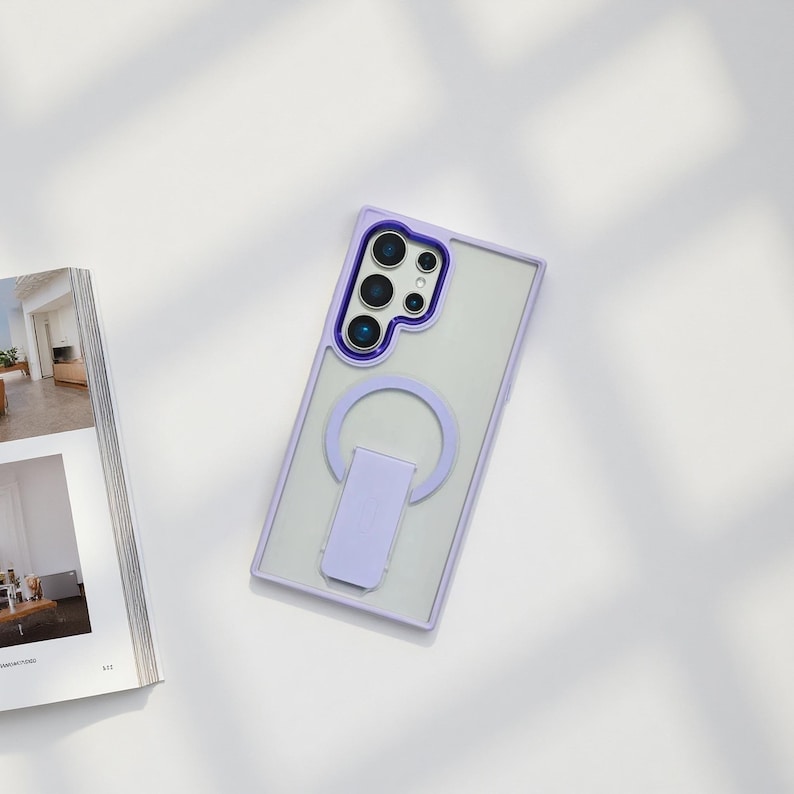 May include: A clear phone case with a purple frame and a matching purple ring holder. The case has a camera cutout and is designed to fit a smartphone. The ring holder can be used as a stand.