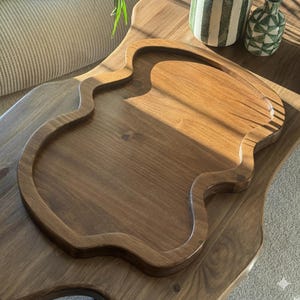 Peut inclure: Un plateau de service en bois de forme organique unique. Le plateau est fait de bois aux tons chauds et présente un bord surélevé. Le plateau est posé sur une grande table en bois. Le plateau est conçu pour servir des aliments ou exposer des objets décoratifs.