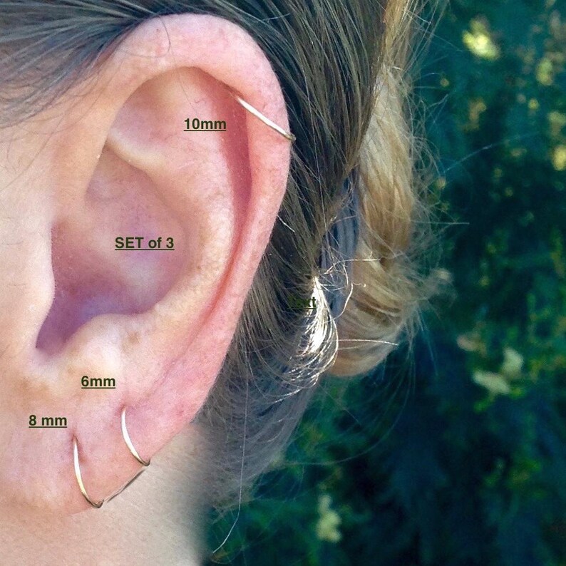 Pu&ograve; includere: Set di tre orecchini a cerchio in argento di diverse dimensioni: 6 mm, 8 mm e 10 mm. Gli orecchini sono mostrati nell'orecchio di una persona.