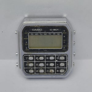 May include: A vintage Casio C-801 calculator watch with a silver-tone case. The watch features a digital display and a keypad with numbers and function buttons. The face of the watch displays the Casio logo and the text "C-801".