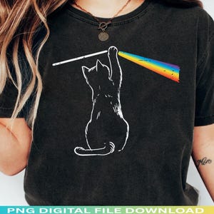 May include: Black t-shirt with a white outline of a cat reaching towards a rainbow prism. The cat is holding a white line that leads to the rainbow. The shirt has the text "PNG DIGITAL FILE DOWNLOAD" at the bottom.
