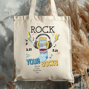 May include: Cream-colored tote bag with the words "ROCK YOUR SOCKS" and a graphic of a sock wearing headphones. The design includes musical notes, lightning bolts, and the date 3.21, celebrating World Down Syndrome Day.