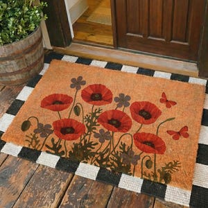 May include: A rectangular doormat with a poppy flower design. The mat features large red poppies with black centers, green stems, and brown leaves. Two red butterflies are also depicted. The mat is bordered by a black and white checkered pattern.