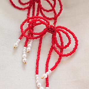 May include: A pair of red beaded earrings with white pearl accents. The earrings are shaped like bows and have long, dangling strands.