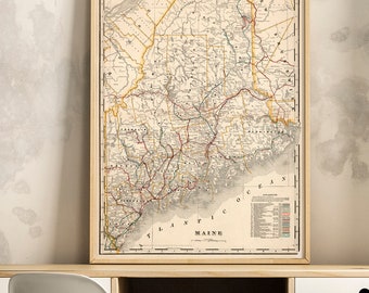 May include: A vintage map of Maine in a wooden frame, hanging above a wooden desk with a white drawer and black metal legs. A white chair sits in front of the desk. A wooden crate sits on the floor below the desk.