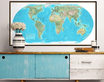 May include: A framed wall map titled Countries of the World featuring a blue ocean and green landmasses. The map is displayed above a rectangular cabinet with two sliding light blue doors and a white drawer with a silver handle.