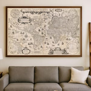 Op de afbeelding: Een ingelijste antieke wereldkaart, getiteld "Nova Orbis Terrarum Geographica", hangt boven een grijze bank. De kaart, gedetailleerd met illustraties en tekst, is geplaatst in een donkerbruine houten lijst. Een ronde houten salontafel en een wit kussen zijn ook zichtbaar.