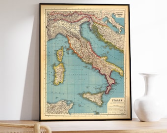 May include: Vintage map of Italy with a blue background and red, yellow, and green borders. The map shows the regions of Italy and includes a small inset map of the island of Sardinia. The map is framed in a black frame and is hanging on a white wall.