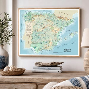 May include: A framed map of Spain, depicting the country's landscape in green, brown, and blue hues. The map features Spanish labels, including the title "España Mapa turística." The frame is made of light-colored wood.