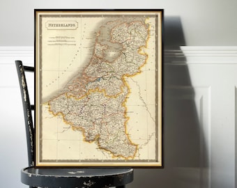 Pode incluir: Um mapa vintage dos Países Baixos, impresso em tinta preta, marrom e verde em papel creme. O mapa está emoldurado em uma moldura preta e é exibido em uma cadeira de madeira preta.