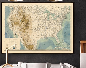 May include: A vintage map of the United States, printed in brown, green, and blue, hangs on a black wall above a white desk with a white chair. The map shows the topography of the country, with mountains, rivers, and lakes.
