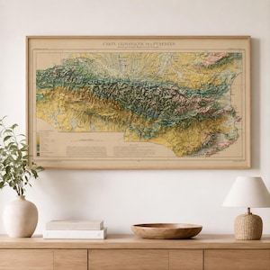 Puede incluir: Un mapa geológico enmarcado titulado Carte Géologique des Pyrénées, que presenta un sombreado topográfico detallado en tonos amarillos, verdes y marrones. La impresión muestra cadenas montañosas, valles y datos geográficos con una leyenda en la esquina inferior izquierda, todo ello dentro de un marco de madera de color claro.