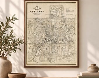May include: A framed vintage map of the city of Atlanta, Georgia, printed on cream-colored paper with black ink. The map displays detailed street grids, railway lines, and a key in the upper right corner, all enclosed in a dark wood frame.