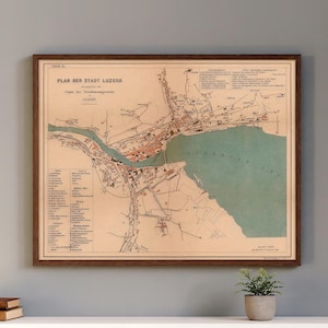 May include: Framed vintage map of Luzern, Switzerland, with text in German. The map features detailed illustrations of the city's layout, including buildings, streets, and the lake. The map is in a wooden frame and is displayed on a white surface.