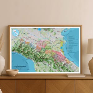 Op de afbeelding: Ingelijste kaart van de wijnregio's Emilia-Romagna in Italië. De kaart toont een 3D-topografische weergave met verschillende kleuren die verschillende gebieden aangeven. Tekst op de kaart bevat de naam van de regio en een websiteadres.