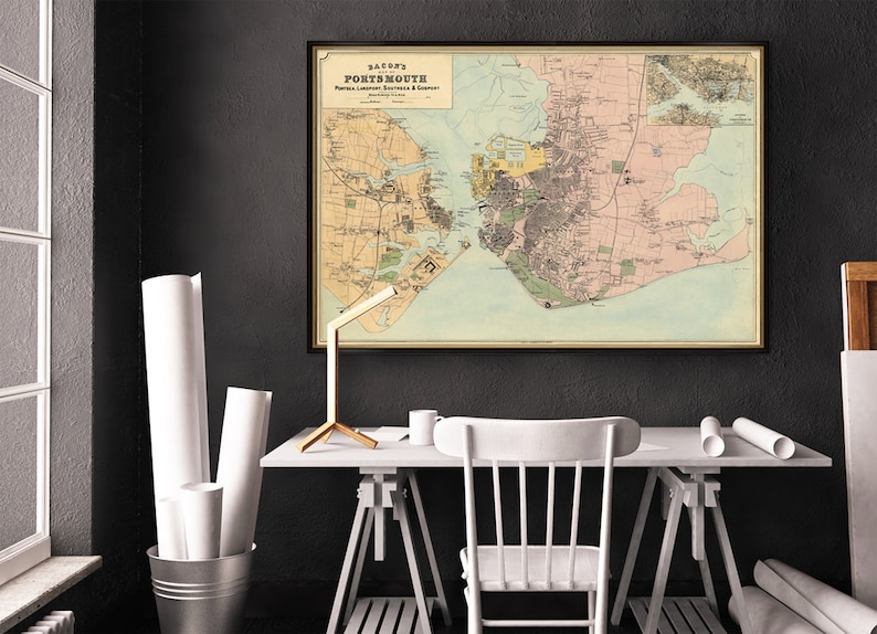 May include: A vintage map of Portsmouth, New Hampshire, framed in black and displayed on a wall in a home office. The map is printed on paper with a cream background and features brown, green, and blue lines and text.