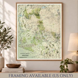 Op de afbeelding: Een ingelijste fysieke kaart van Arizona met topografische reliëfschaduwen in tinten groen en beige. De kaart toont namen van provincies, grote steden en geografische kenmerken, met de tekst Physical Map of Arizona onderaan.