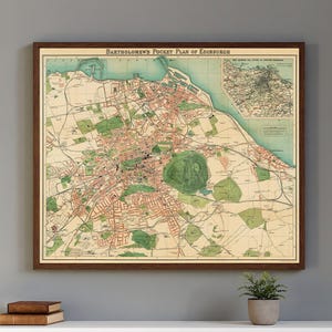 May include: Framed vintage map of Edinburgh, Scotland, titled "Bartholomew's Pocket Plan of Edinburgh." The map features a detailed street layout with green, red, and beige tones, and a smaller inset map. The frame is a dark brown color.