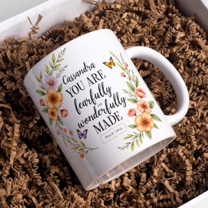 May include: White ceramic mug with floral and butterfly illustrations. The mug features the text "Cassandra YOU ARE fearfully and wonderfully MADE" and "PSALM 139:14". The mug is packaged in a white box with brown paper filler.