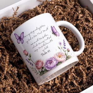 May include: White ceramic mug featuring a floral design with pink and purple flowers, lavender, and two purple butterflies. The mug has the text "He is my refuge and my fortress, my God, in Him I trust. Psalm 91."