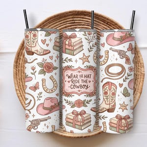 May include: Three white insulated tumblers with black straws, featuring a repeating pattern of cowboy boots, hats, horseshoes, and roses. The center tumbler has the text "Wear the Hat Ride the Cowboy."