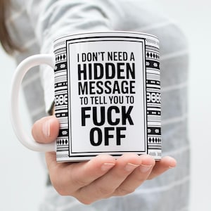 May include: White ceramic mug with a black and white geometric pattern and the text "I DON'T NEED A HIDDEN MESSAGE TO TELL YOU TO FUCK OFF" in bold black letters. The mug has a white handle.