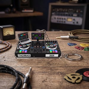 May include: A clear acrylic keychain shaped like a DJ controller with two jog wheels, colorful performance pads, a laptop, and a screen. The front features the text THOMAS and 2026 printed in black on white rectangular labels. A metal ring is attached.