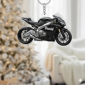 May include: A black motorcycle keychain with the name "David" printed on the side. The keychain is made of clear acrylic and has a silver keyring attached. The motorcycle has detailed features, including wheels, a seat, and a windshield.