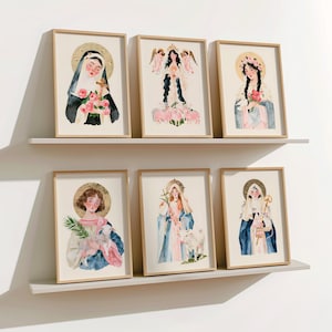 Könnte beinhalten: Sechs gerahmte Aquarelldrucke von religiösen Figuren. Jeder Druck zeigt einen anderen Heiligen mit Heiligenschein, Blumen und Tieren. Die Kunstwerke werden auf zwei weißen Regalen vor einer weißen Wand ausgestellt. Die Rahmen sind hellbraun.