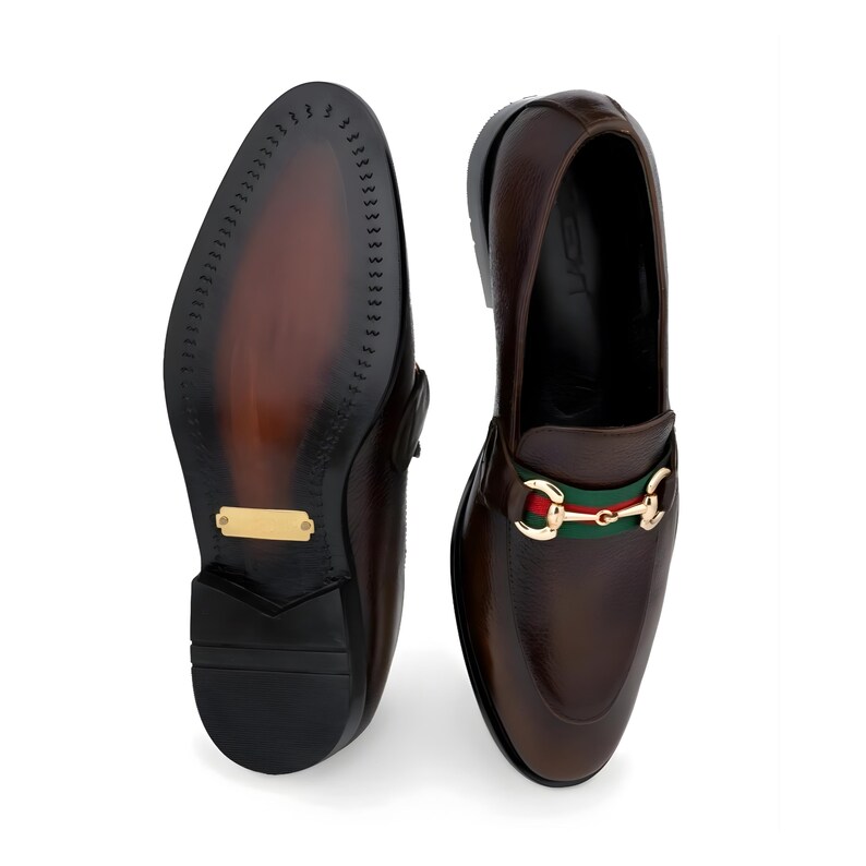 May include: A pair of brown leather loafers with a gold-colored buckle and green and red stripe detail. The sole of one shoe is visible, showing a dark brown sole with a gold-colored plate.