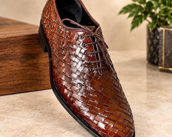 May include: A brown leather oxford shoe featuring a woven basket-weave pattern across the upper. The shoe includes matching brown laces, a rounded toe, and a dark sole. The leather has a polished finish with visible texture from the weave.