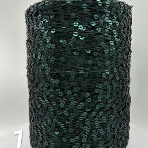 以下が含まれることがあります： 濃い緑色のスパンコールトリムの糸巻き。スパンコールは丸く、密に詰め込まれており、光沢のある質感の表面を作り出しています。糸巻きの上部は濃いグレーで、側面には数字の「1」が見えます。