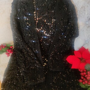 May include: A black sequined cardigan. This open-front knitted sweater has long sleeves and a loose fit. The garment is embellished with small, reflective sequins. The cardigan is a stylish piece of clothing.
