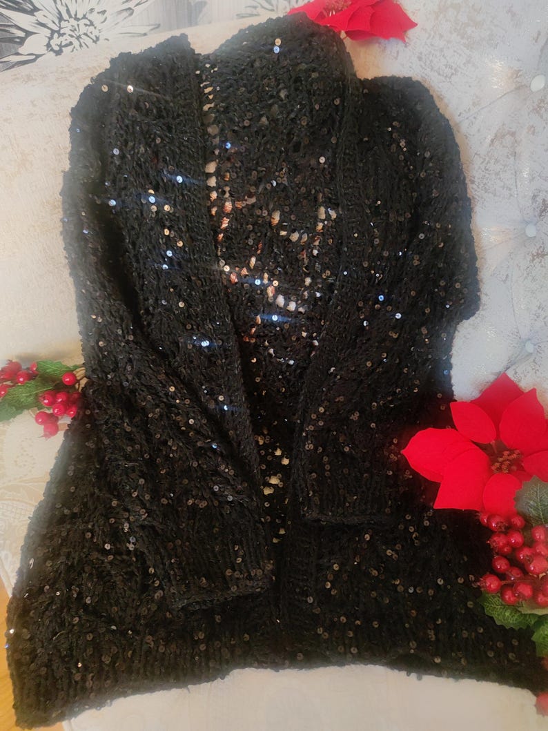 May include: A black sequined cardigan. This open-front knitted sweater has long sleeves and a loose fit. The garment is embellished with small, reflective sequins. The cardigan is a stylish piece of clothing.