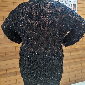 May include: A black, open-weave cardigan with long sleeves and sequin detailing. The cardigan has a relaxed fit and is made from a soft, lightweight fabric. This garment is ideal for layering and adds a touch of glamour to any outfit.