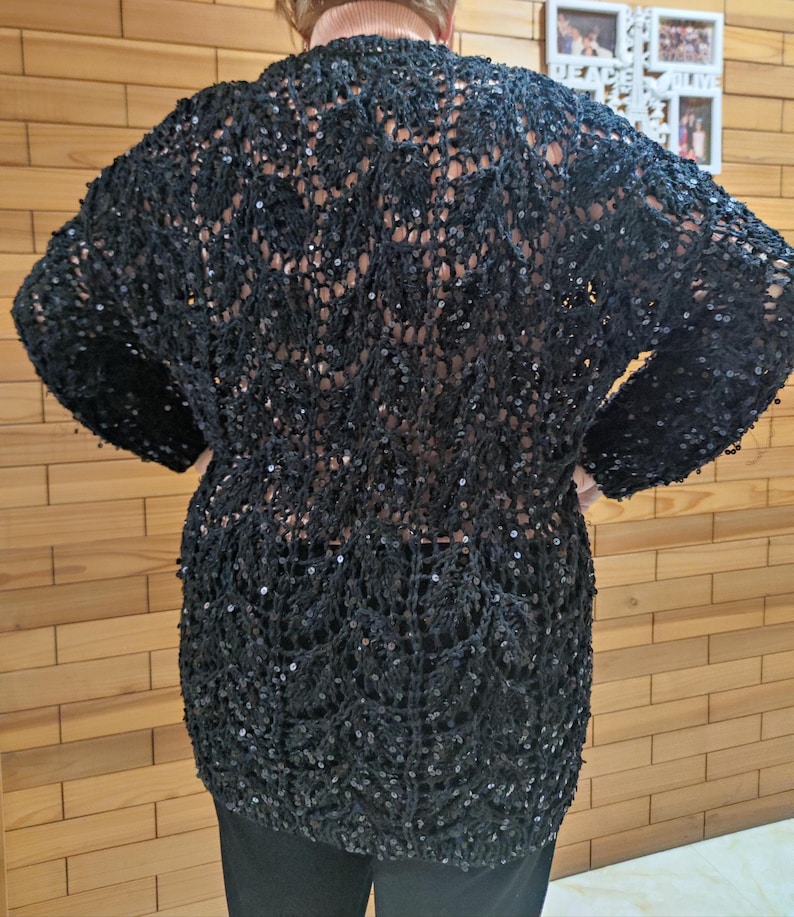 May include: A black, open-weave cardigan with long sleeves and sequin detailing. The cardigan has a relaxed fit and is made from a soft, lightweight fabric. This garment is ideal for layering and adds a touch of glamour to any outfit.