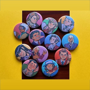 Può includere: Una collezione di spille rotonde e colorate con illustrazioni di personaggi in stile anime. I bottoni hanno una finitura lucida e sono disposti su una superficie di legno scuro su uno sfondo giallo.