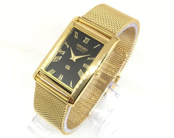 Reloj de pulsera Seiko SQ Quartz Tank vintage: esfera romana, correa de acero inoxidable, negro y dorado.